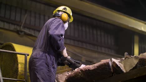 plant worker breaks chunks of metal waste with large sledgehammer