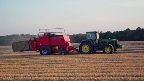 ernte von trockenem gras. landwirtschaftliche arbeiten auf dem feld. traktor drückt heu in quadratische balen auf dem natürlichen gelben feldhintergrund.