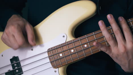 artist plays white bass guitar on different frets closeup