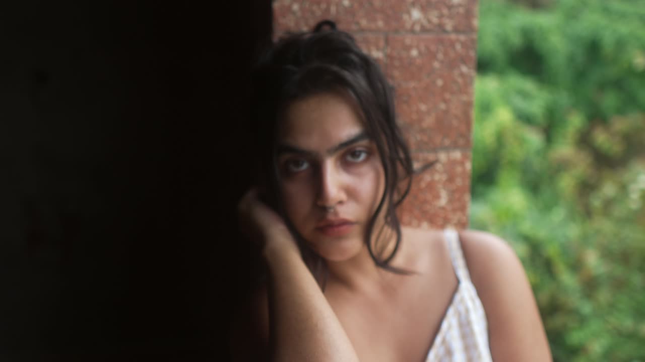 Mujer joven apoyada en un pilar con expresión pensativa, mirando a la cámara.