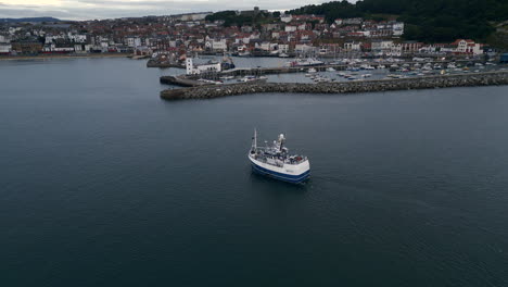 establishing drone shot of scarborough harbour with fishing boat heading inland