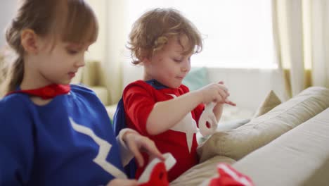 Mittlere-Nahaufnahme-Von-Kindern,-Die-Superhelden-Augenmasken-Aufsetzen-Und-Laut-Lachen,-Während-Die-Eltern-Auf-Verschwommenem-Hintergrund-Sprechen