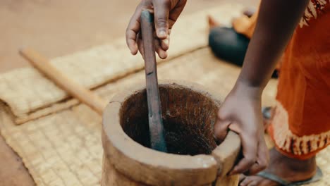 una dama africana usa un utensilio de madera para aflojar el café molido en un gran mortero de madera