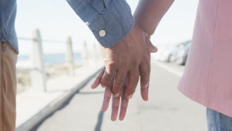 close up of senior african american couple holding hands on promenade by the sea, slow motion