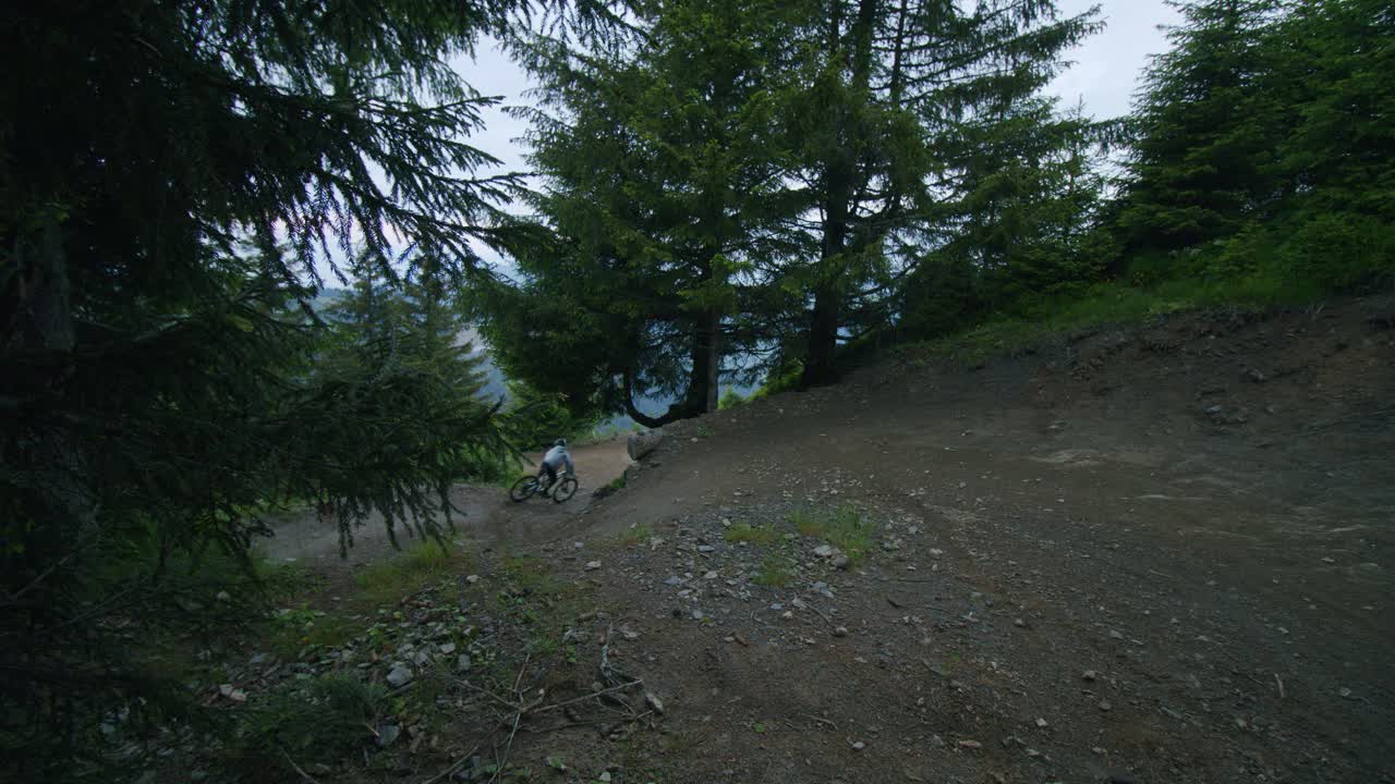 산악 자전거 타는 사람은 모퉁이를 자르고 어두운 숲에서 점프를 합니다.