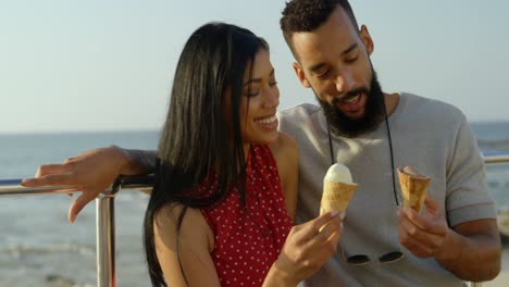 feliz pareja de raza mixta de pie con conos de helado en el paseo marítimo 4k