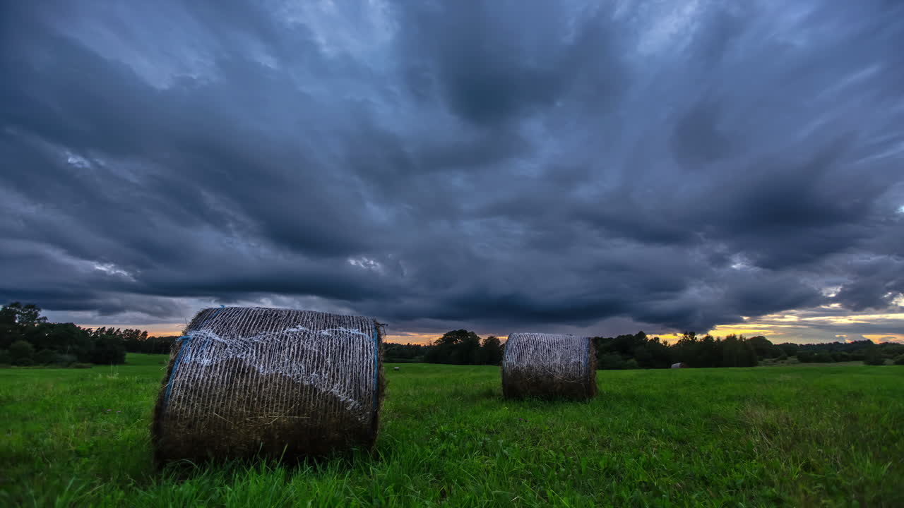 Stormfulde skyer ruller ind over landbrugsland med høballer på enge