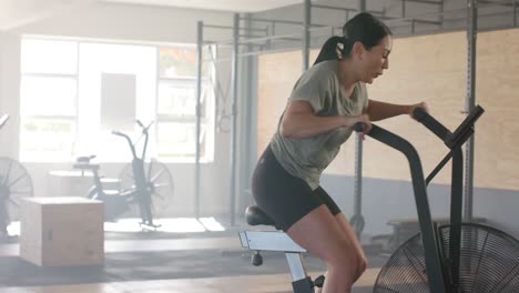 determined unaltered caucasian woman training on elliptical bike at gym, copy space in slow motion