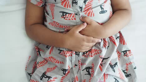 a young girl holding her stomach in pain, lying on a bed