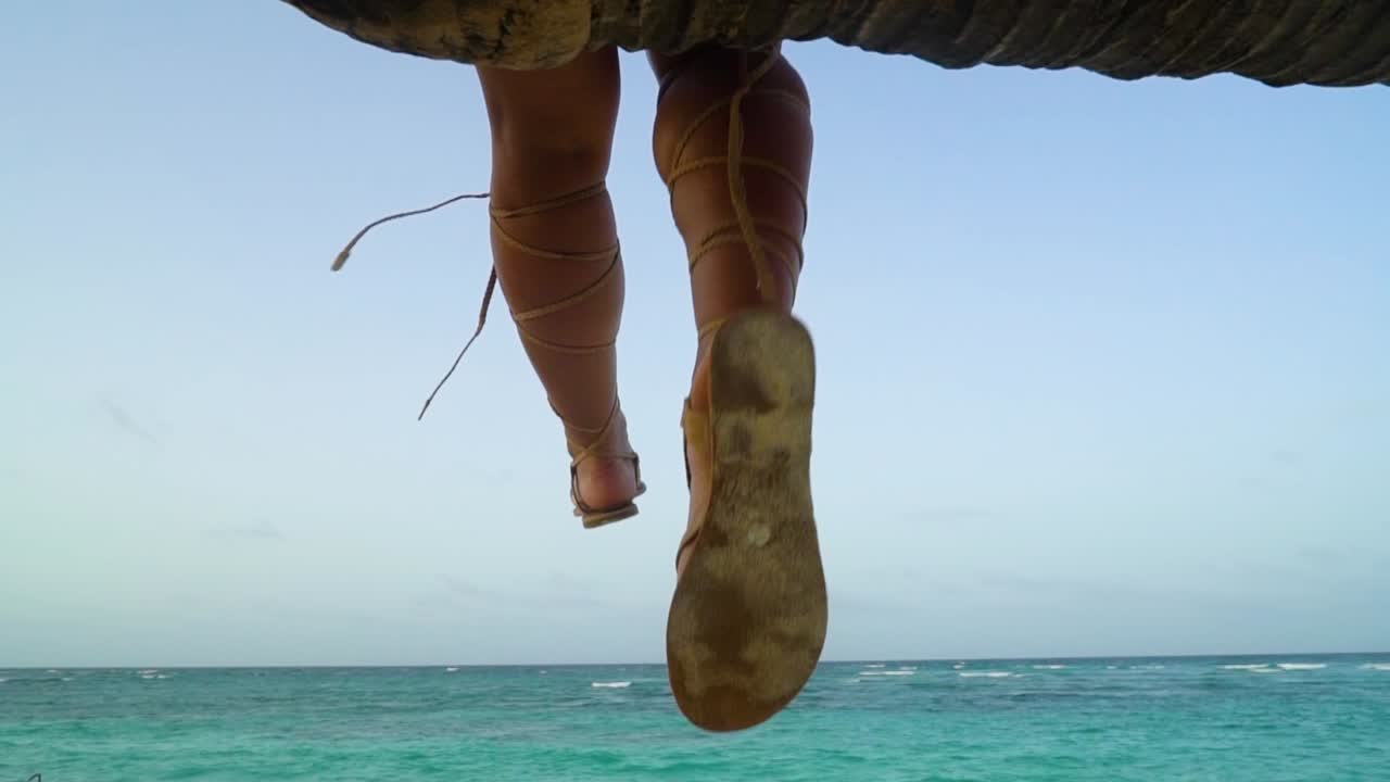 A girl sitting on the palm tree hanging her beautiful legs of the tree