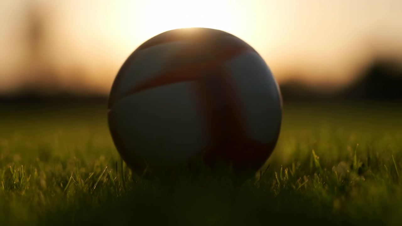 En ball som hviler på gress på en eng med en solnedgangshimmel, sett fra en lav vinkel som ser opp på ballen, en fredelig utendørs rekreasjonsscene med sportsutstyr av gummi eller plast, rolig