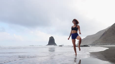 engaging in stretching and yoga, a young woman stands by the ocean's edge and gazes into the distance in slow motion
