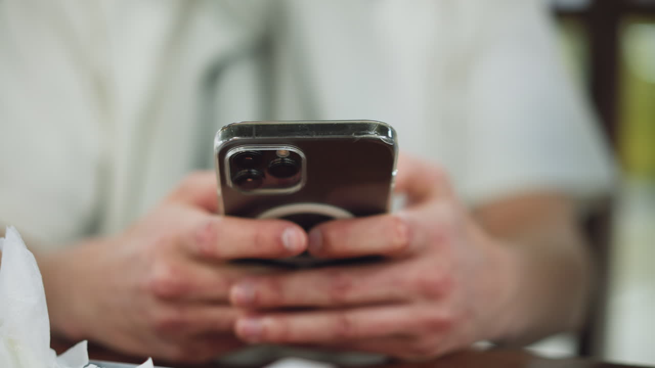White man hand showing some reddish knuckles holding black apple phone in clear pouch while pressing screen closeup, soft background blur, focus on beauty, gesture and protective case