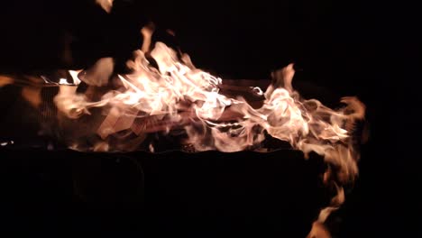 la hoguera con combustible de madera arde rápidamente emitiendo calor y luz sobre las brasas incandescentes en el fondo, tiro bloqueado en primer plano en la oscuridad de la noche, galicia, españa