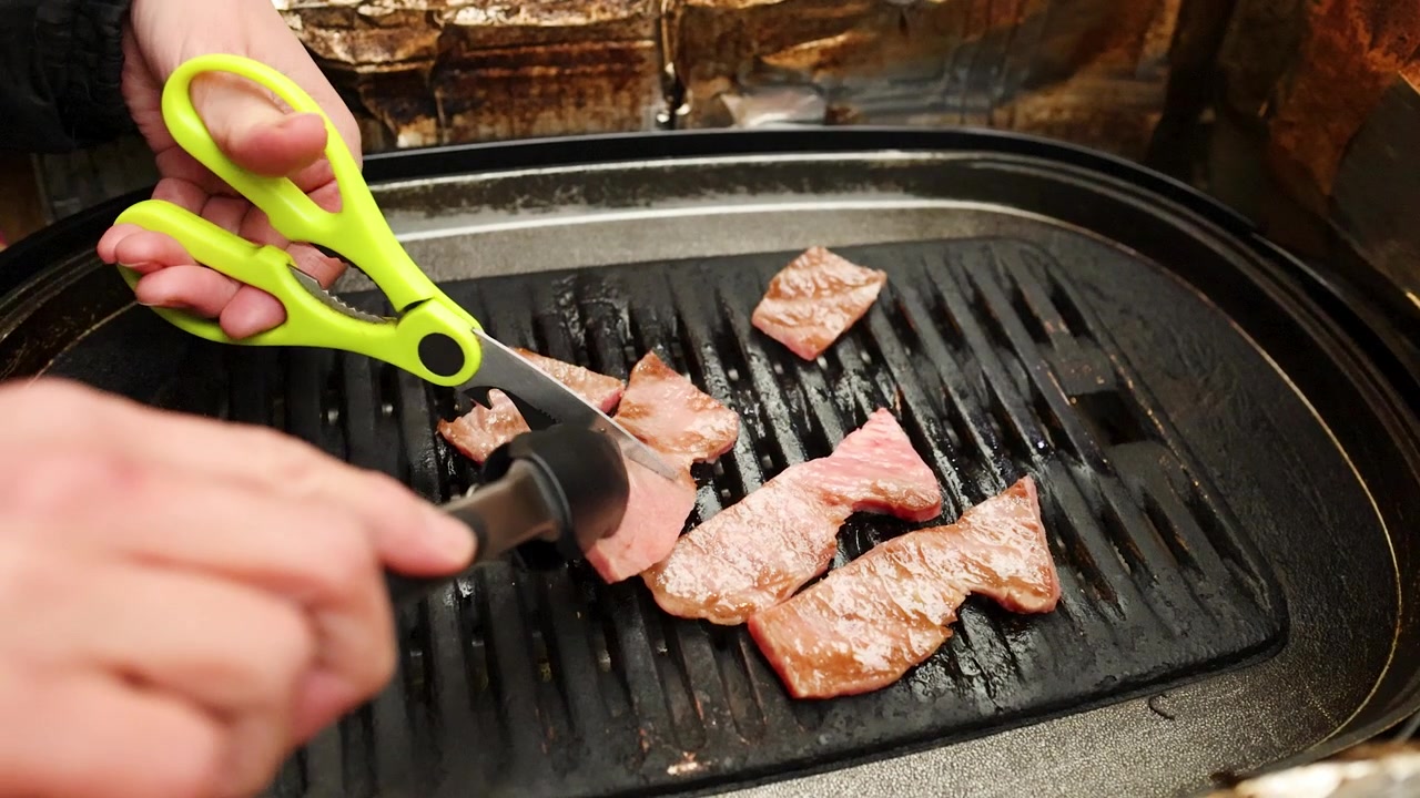 Primo piano delle mani che usano forbici e pinze per tagliare carne di Wagyu su una griglia
