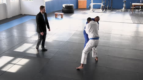practicing judo, two men sparring on mats with coach observing