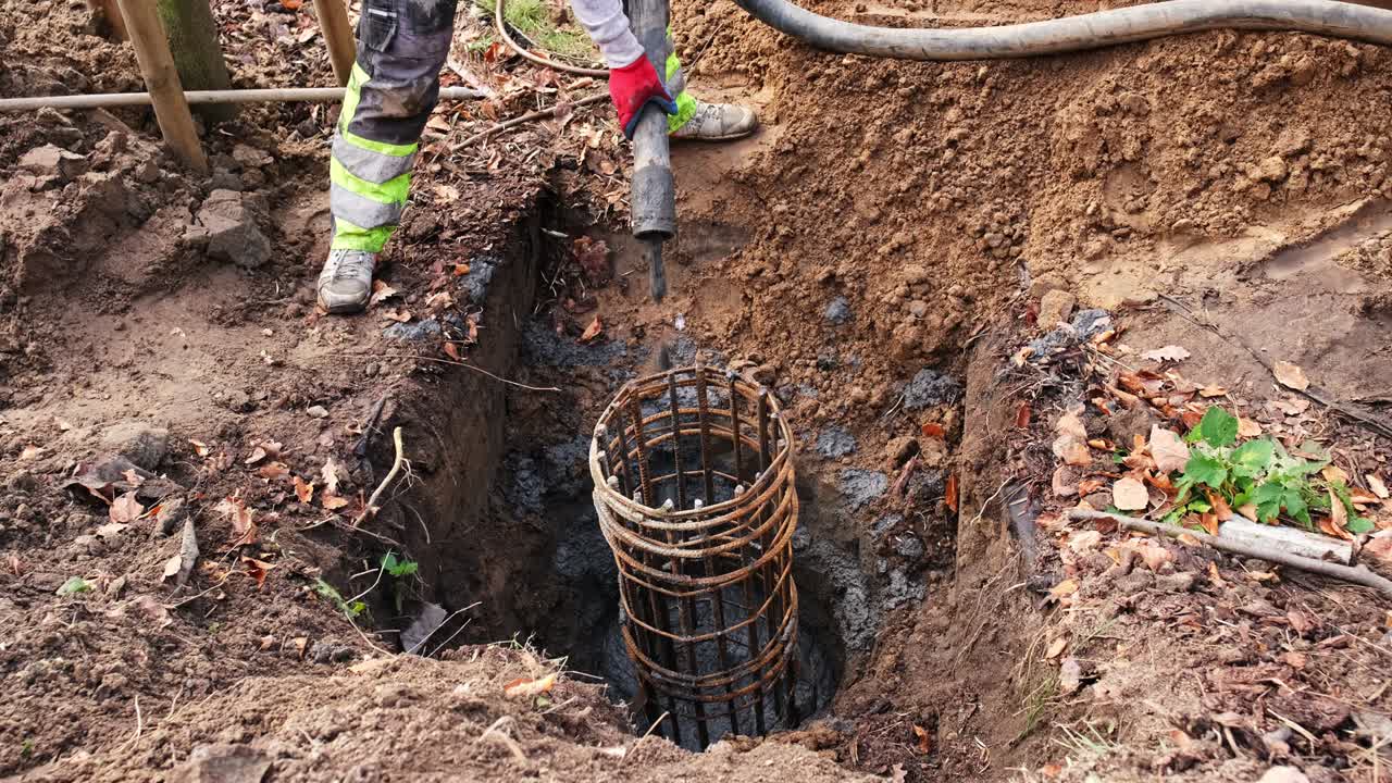 trabajador de la construcción vertiendo cemento líquido de la tubería llenando la excavación de cimientos de hormigón con barras metálicas reforzando la jaula
