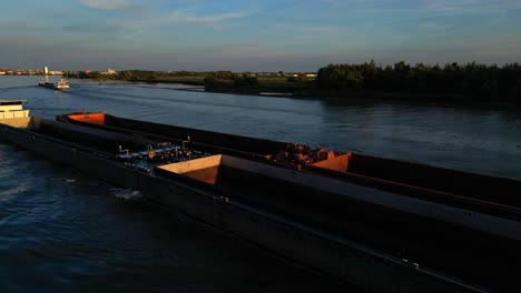 Luftorbitalansicht-Des-Nautischen-Verkehrs,-Langes-Frachtkahn-Binnenschiff,-Das-Bei-Sonnenuntergang-Entlang-Des-Flusskanals-In-Zwijndrecht-Niederlande-Navigiert,-Küstennavigation-Und-Transport