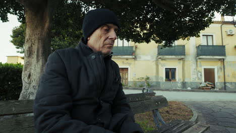 retired elderly man feeding food to birds sitting in bench in square of city