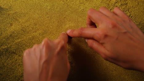 person drawing shape of heart on golden glitter 4k