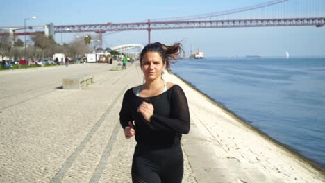 Focused-young-woman-in-sportswear-running-near-river