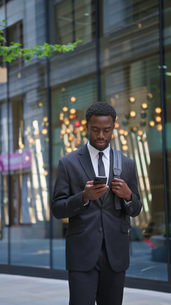 Vertical Video Shot Of Young Businessman Wearing Suit Using Mobile Phone Walking Outside Past Offices In The Financial District Of The City Of London UK Shot In Real Time 1