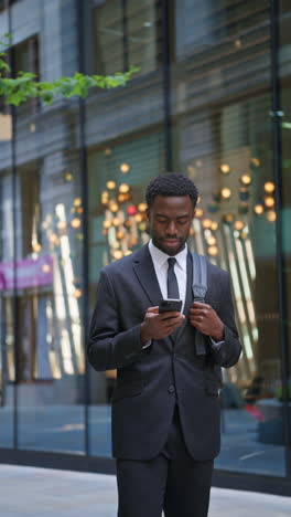 vertical video shot of young businessman wearing suit using mobile phone walking outside past offices in the financial district of the city of london uk shot in real time 1