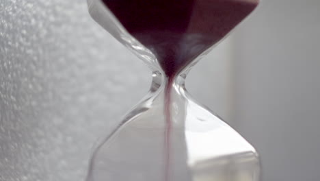 extreme close up view of pink sand particles flowing through an hourglass