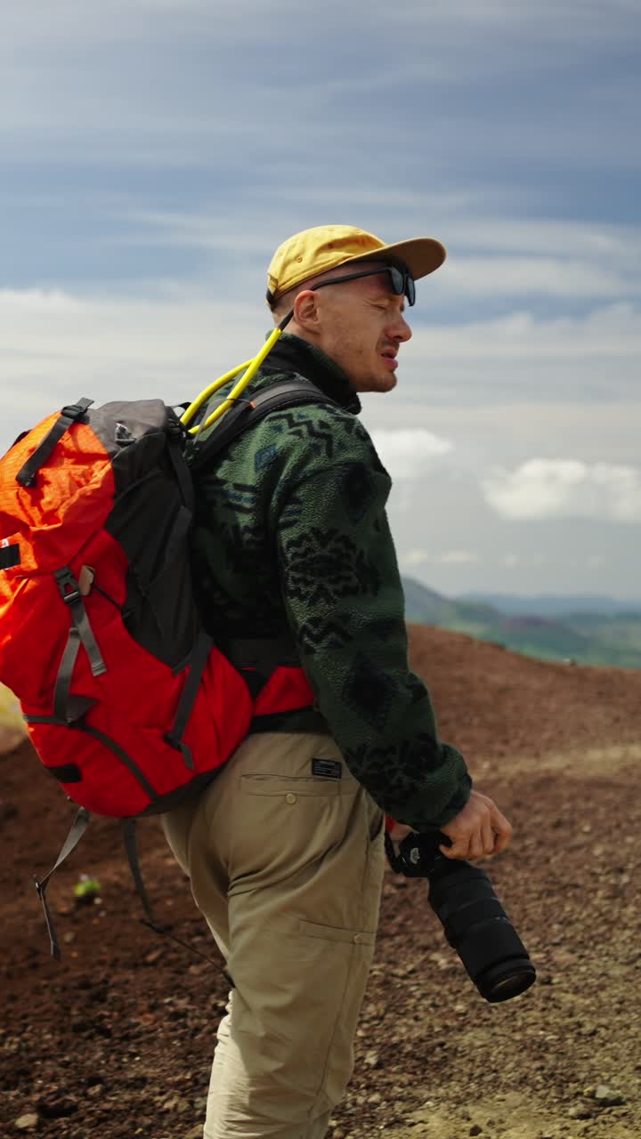 Hombre haciendo senderismo por un sendero de montaña con mochila y cámara.