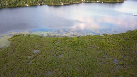 4K-Luftaufnahme-Vom-Land-über-Einen-Kanal-Und-Feuchtgebiete-Zum-See-Mit-Blauem-Wasser-Und-Grünen-Bäumen-Bei-Sonnigen-Sommerbedingungen,-Mitten-In-Michigan-Am-Cranberry-Lake,-In-Der-Nähe-Von-Harrison,-Michigan