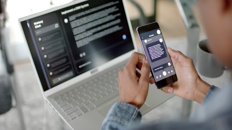 African american businessman using smartphone and laptop with ai chatbot at home, slow motion