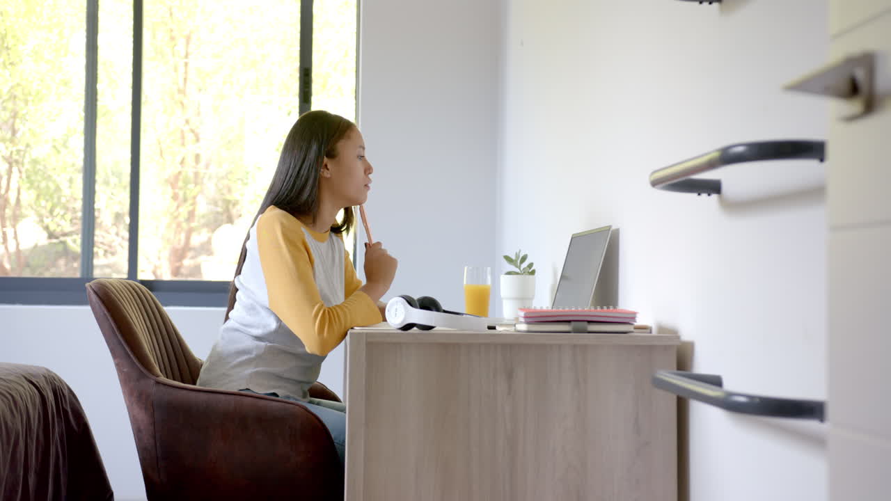 Studying at desk, girl using laptop with notebook and orange juice nearby