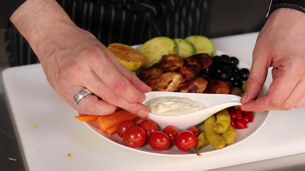Chef preparing a platter of chicken wings and vegetables