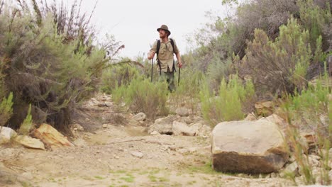 caucasian male survivalist enjoying trekking through wilderness with backpack and walking poles