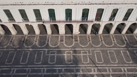 Cinematic-aerial-tracking-shot,-flock-of-birds-flying-above-Cordoba-Cabildo-colonial-town-hall-with-elegant-15-arch-passageway-and-building-blueprint-mirroring-on-the-ground-at-San-Martin-plaza