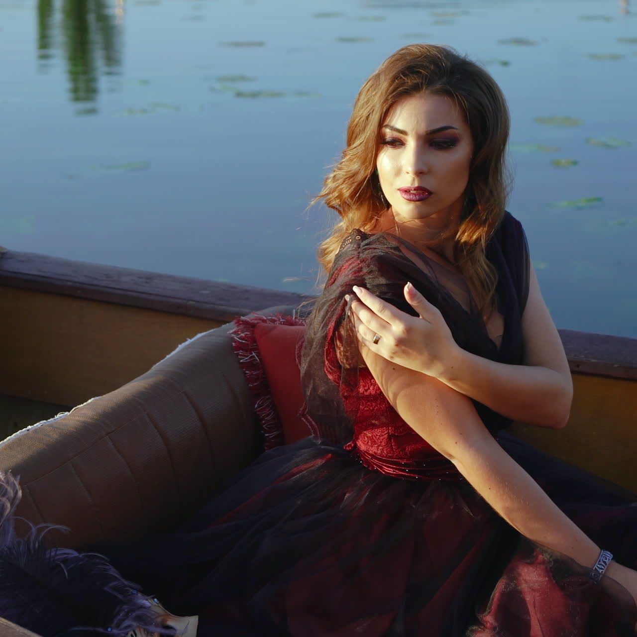 Luxury young woman wearing elegant carnival dress floating in gondola on the water background. Fantastic female with long hair and pretty makeup sitting in a boat.