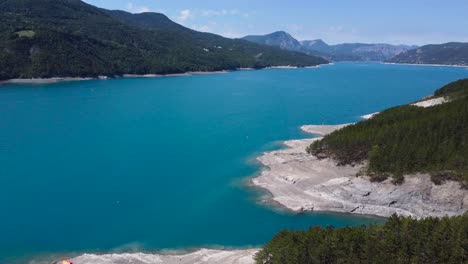 A-tilting-drone-shot-revealing-a-crystal-blue-lake-surrounded-by-mountains-in-Southern-France