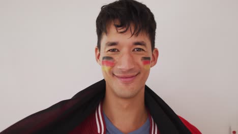 Portrait-of-happy-biracial-man-with-national-flag-and-flag-of-germany-on-cheek