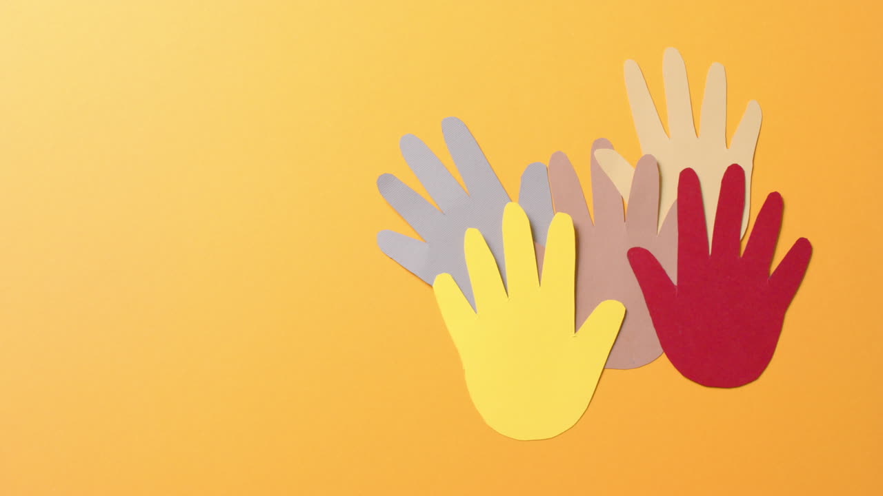 복사 공간과 함께 오렌지색 배경에 다채로운 종이로 만들어진 손을 가까이 붙입니다.