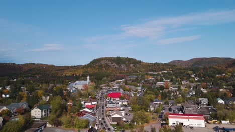 saint-sauveur town within les pays-d'en-haut regional county municipality, quebec canada , main road traffic and mountain covered in orange foliage during fall season aerial