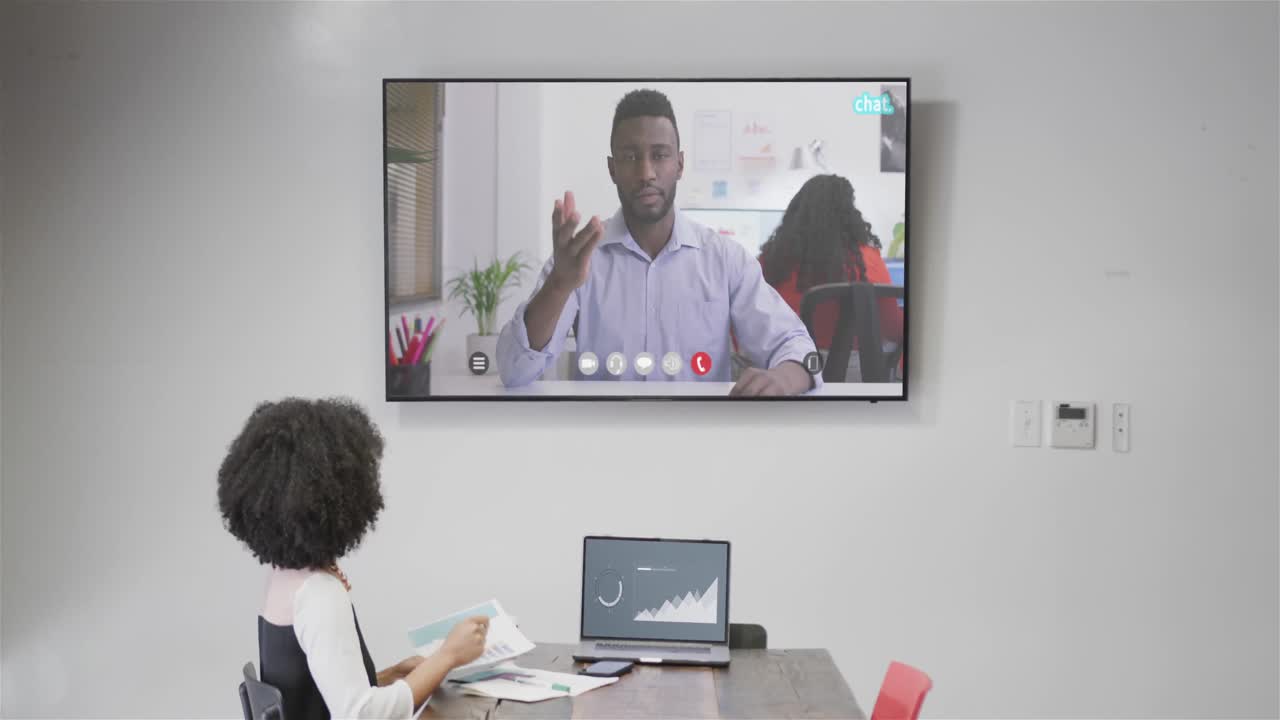 mujer de negocios afroamericana en videoconferencia con su colega afroamericano en la pantalla de televisión