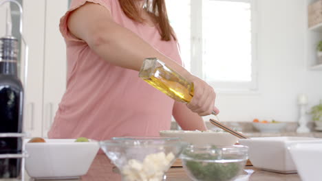 Feliz-Mujer-Birracial-De-Talla-Grande-Aderezando-Ensalada-Con-Aceite-De-Oliva-En-La-Cocina,-Espacio-Para-Copiar,-Cámara-Lenta