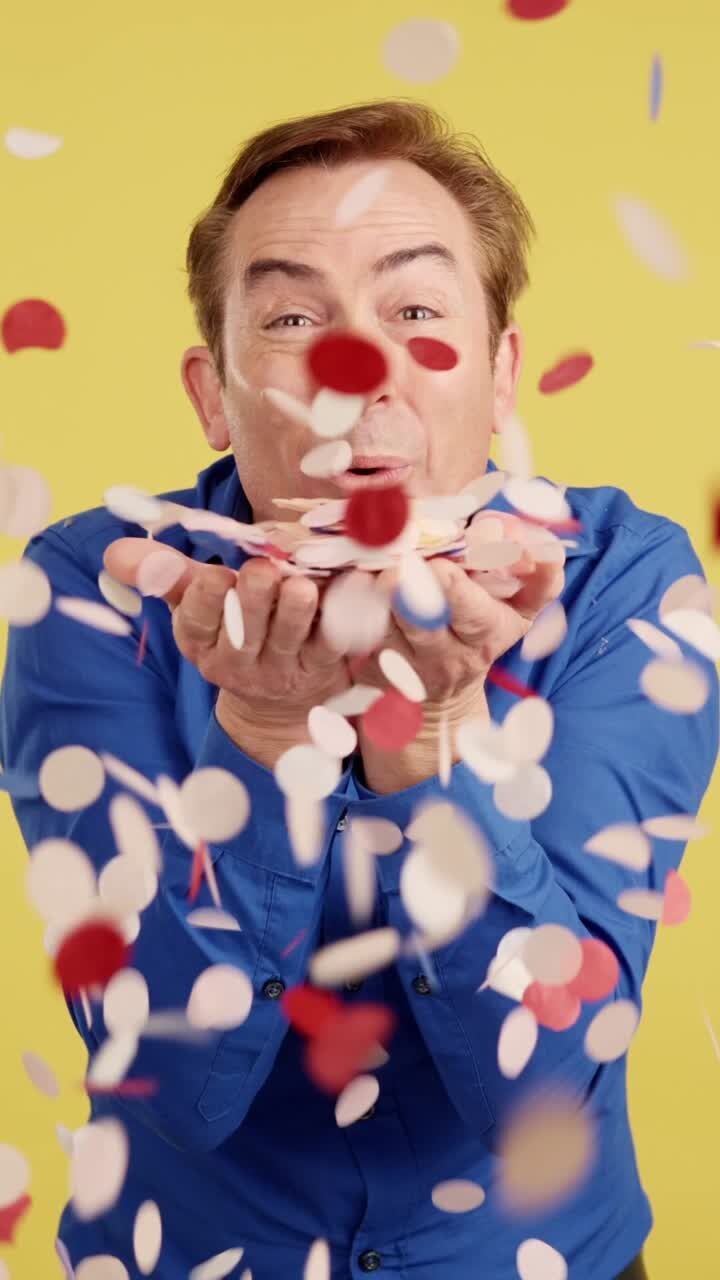 Happy Man Blowing and Throwing Confetti on a Yellow Background