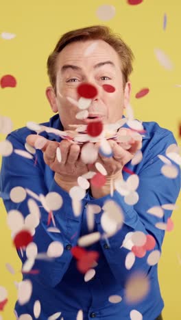 happy man blowing and throwing confetti on a yellow background