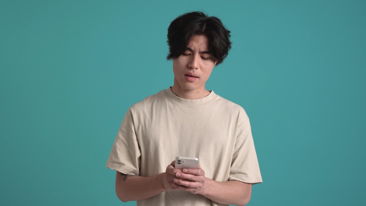 Displeased Asian man texting by phone