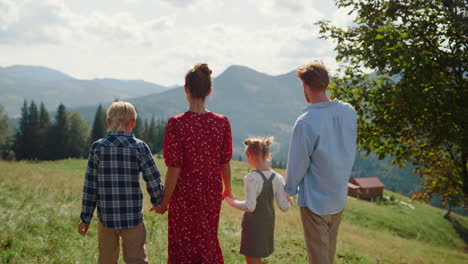 back view friendly family spending holiday in mountains. parents walking kids.