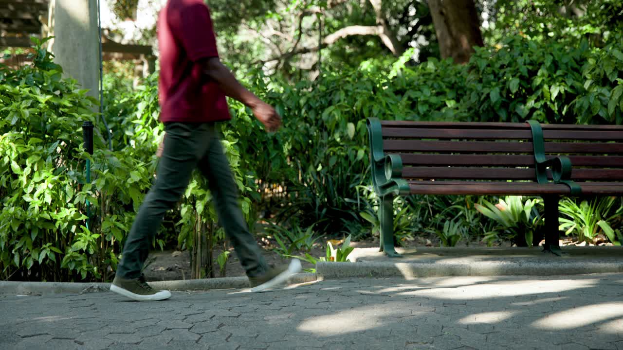 Fotgjengere kommer inn fra venstre kant og går forbi en tom benk på en skyggefull parksti.