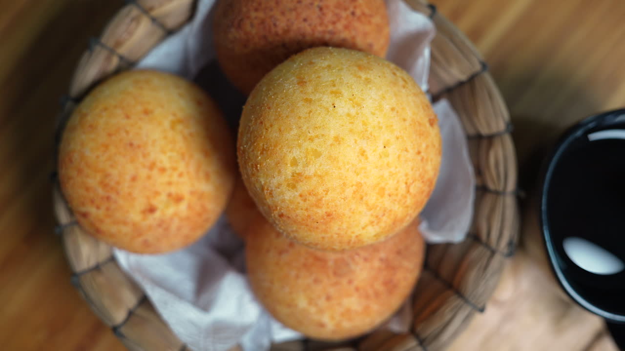 Close-up of freshly baked Colombian almojábanas in a rustic basket. Warm tones, soft lighting highlight the cheese bread's texture. A cozy and appetizing visual