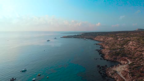 aerial view slowly dropping down to ground level over konnos bay with boats anchored in the water