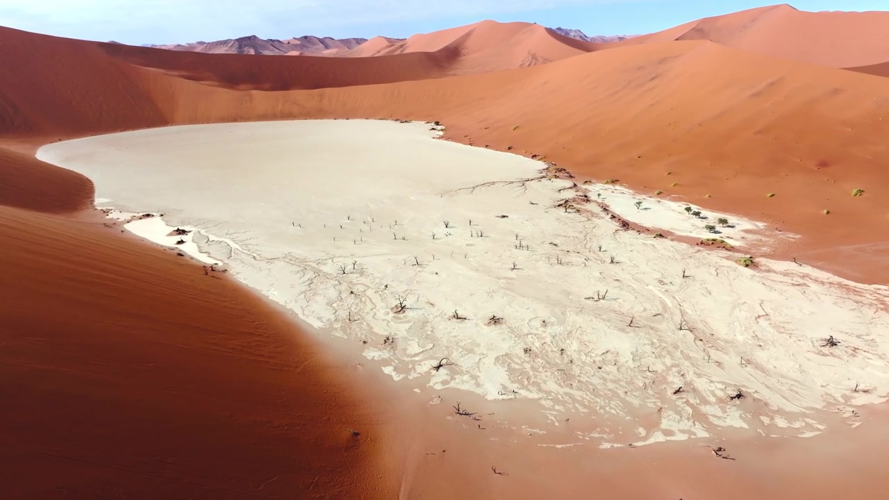 Tomada aérea de drone de Deadvlei no mar de dunas de Sossusvlei. As imponentes dunas vermelhas brilham contra as planícies de argila pálida e rachada desta antiga paisagem desértica selvagem. Vista alta das famosas árvores mortas de cima